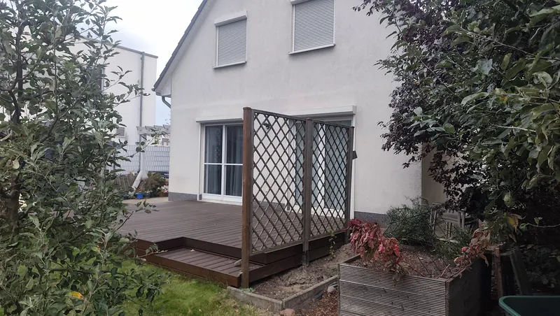 Seitliche Ansicht der offenen Hochterrasse mit Stufen und Rankgitter vor der Überdachung