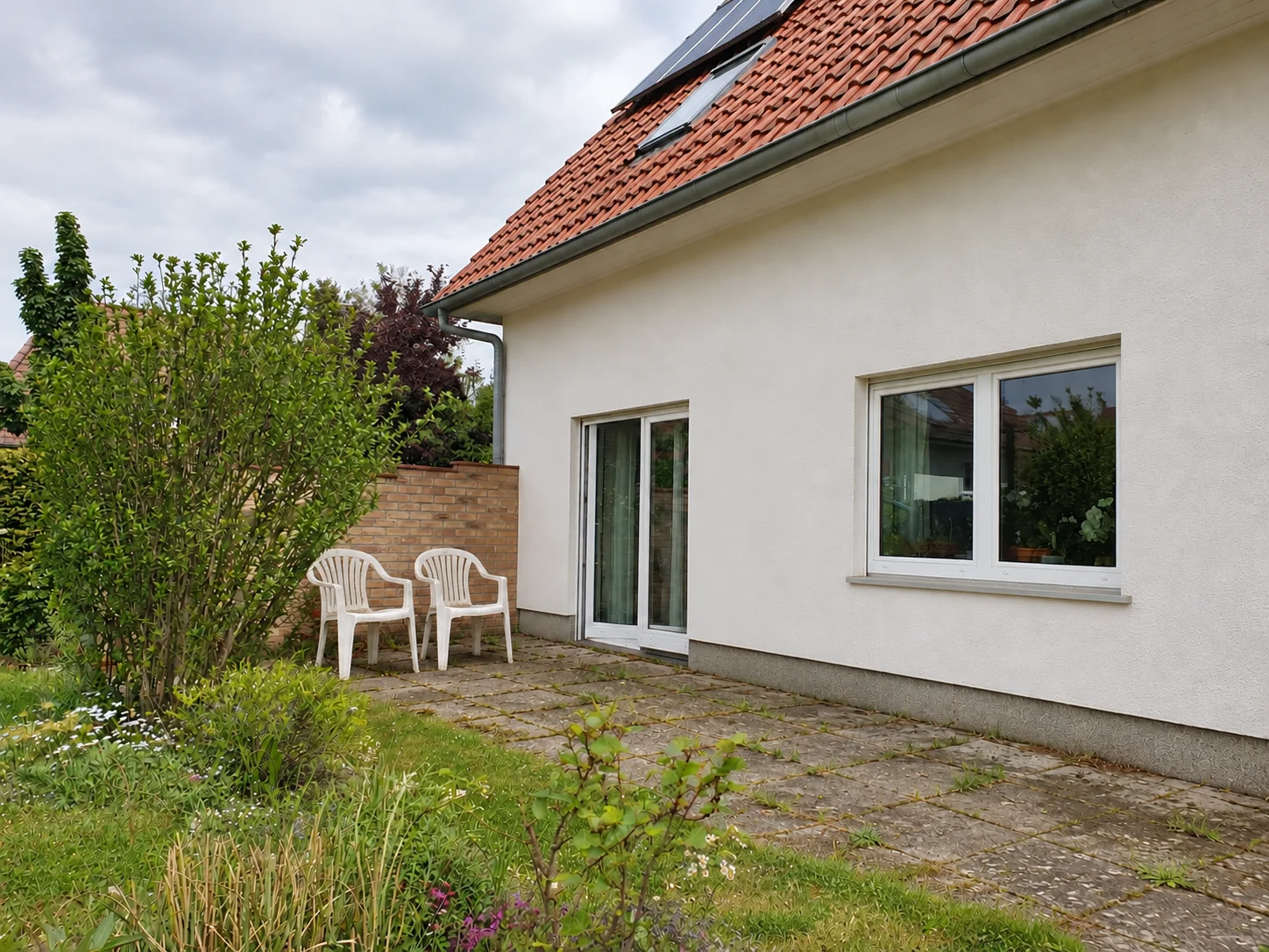 KI-Vorherkonzept am eigenen Hausfoto: alte Terrasse ohne Dach, Rasen und zwei weiße Plastikstühle
