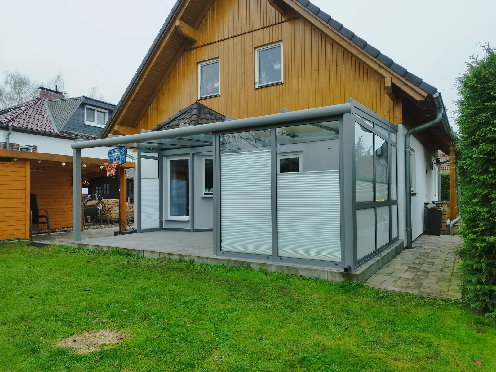 Eigener verglaster Terrassenbereich mit teilweise hochgezogenen weißen Plissees in den Seitenfeldern