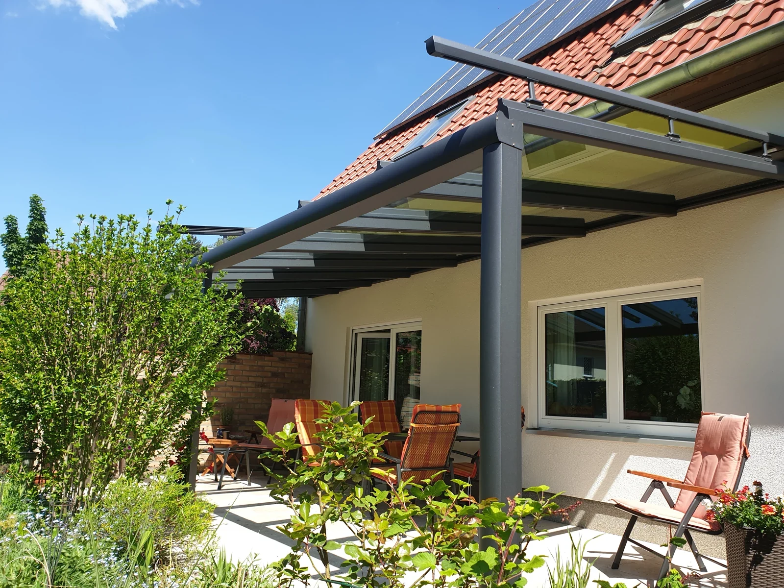 Dunkle Aluminiumkonstruktion an heller Fassade neben begrüntem Garten