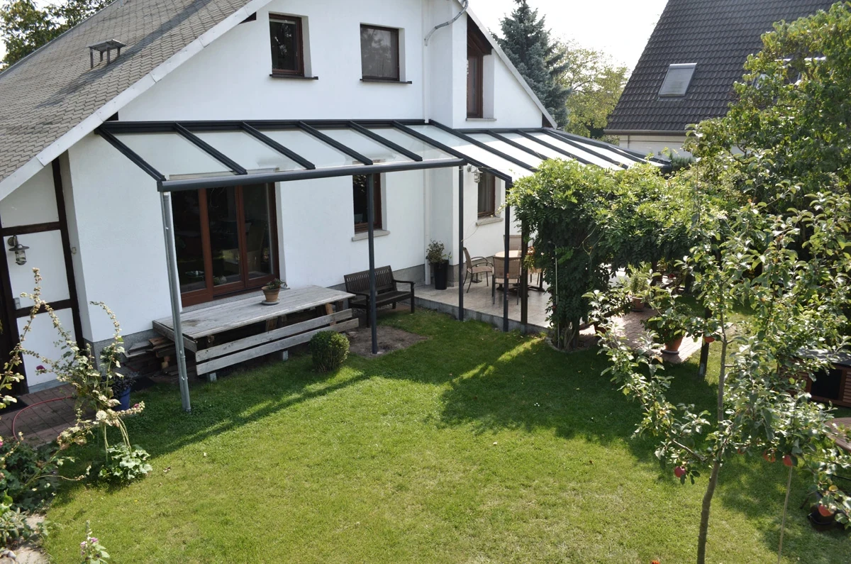 Eigenes Karalus-Terrassendach an weißem Giebelhaus, mit Glasflächen und Garten
