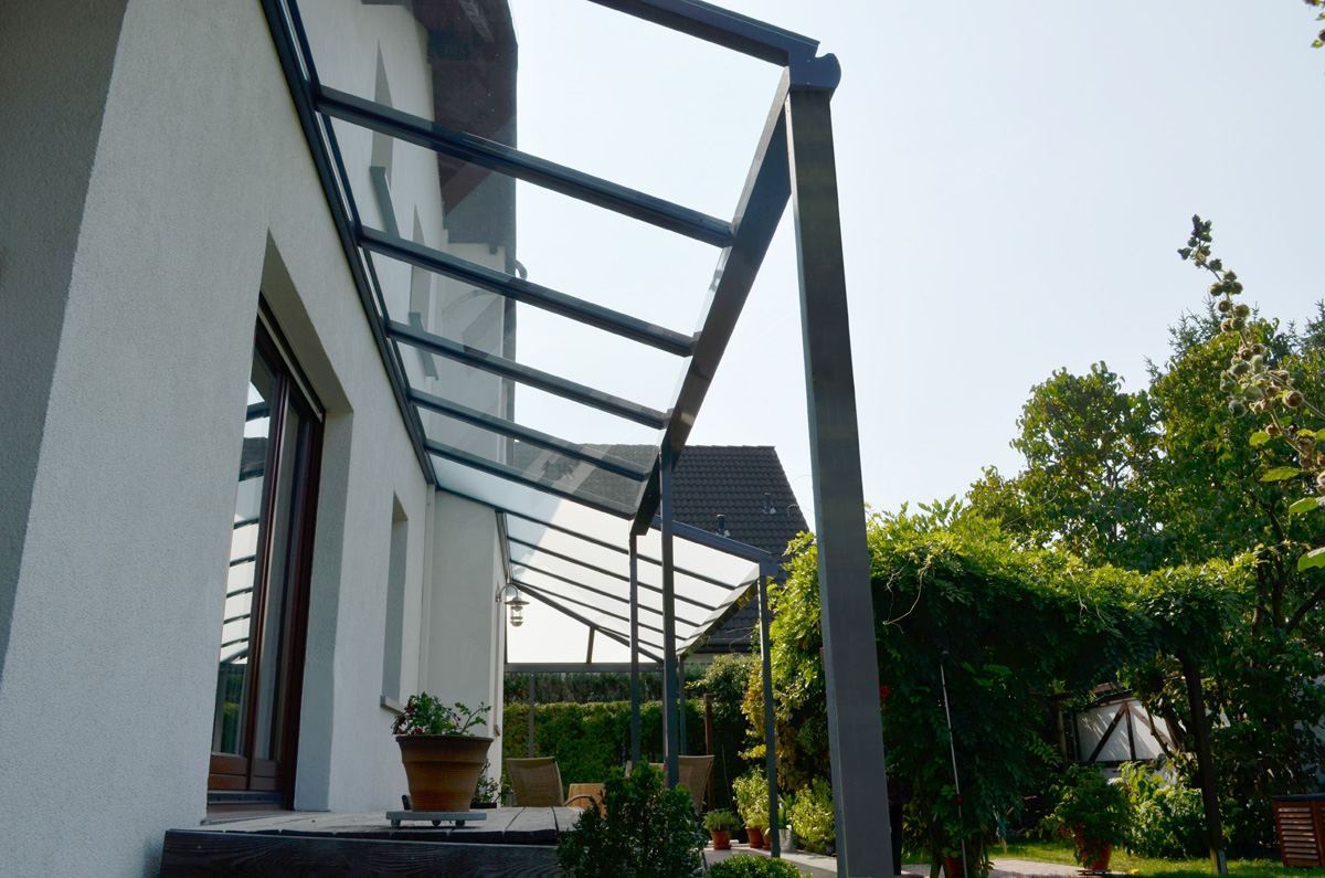 Offenes Terrassendach mit dunklen Aluminiumprofilen und Glasdach an weißer Hauswand
