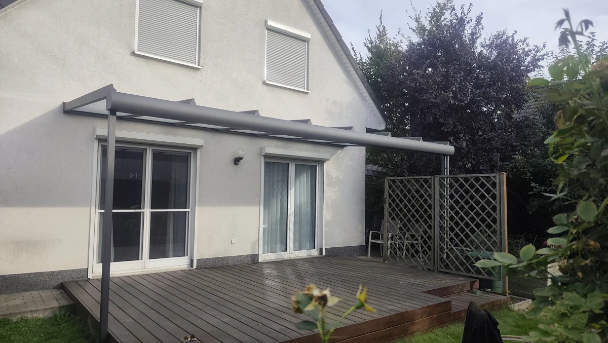 Die fertige Überdachung vom Garten aus. Zwei Frontstützen tragen das 5,80 × 3,00 Meter große Dach in DB 703. Die vorhandene Terrasse und das Rankgitter bleiben erhalten; das Fallrohr liegt sichtbar neben der rechten Stütze. Projekt in 12557 Berlin-Köpenick.