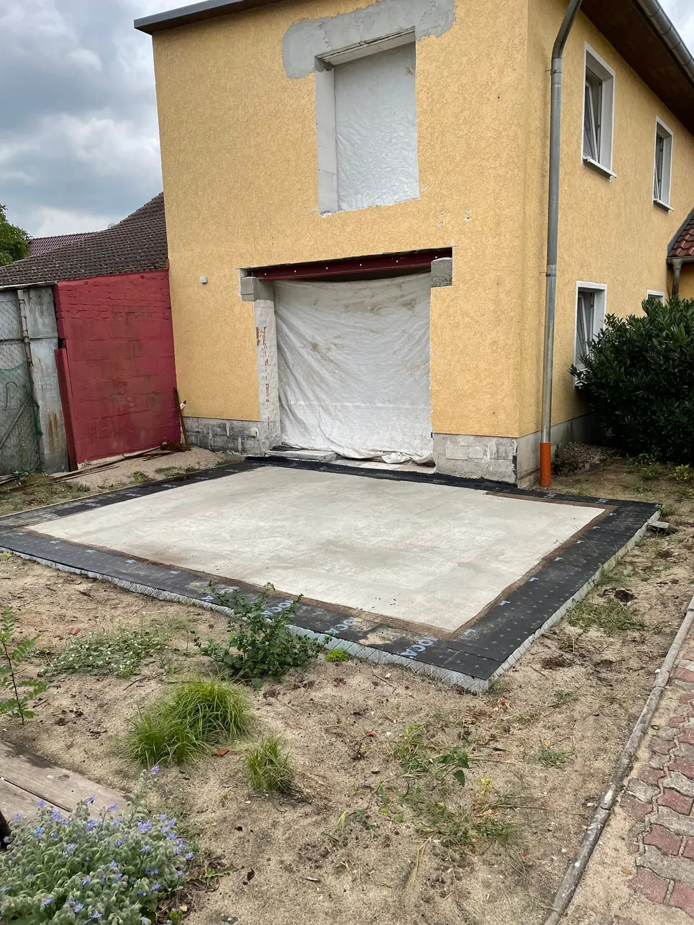 Bauphase: vorbereitete Bodenplatte und abgedeckte Öffnung in der Hauswand.